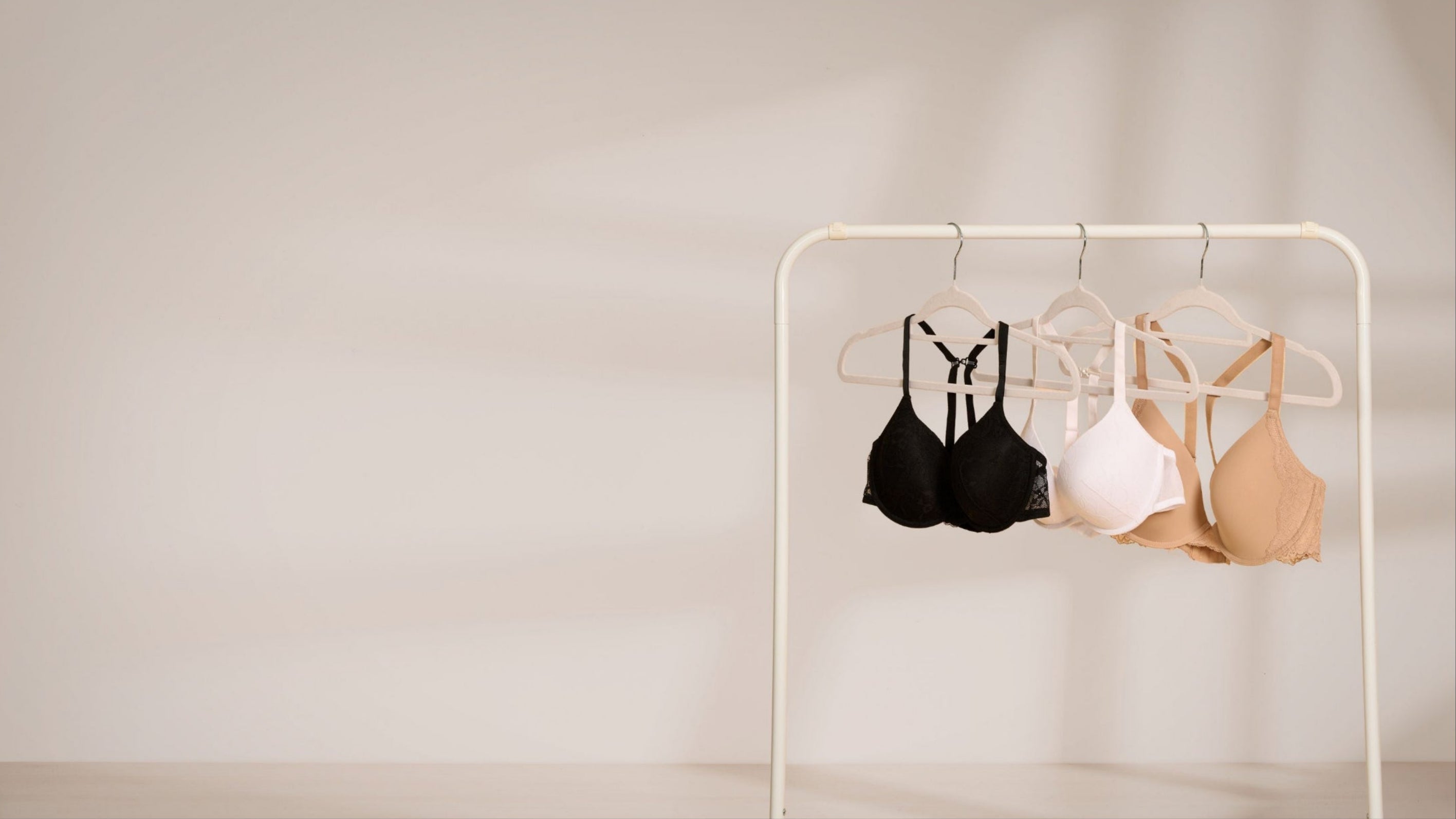 Three bras with THE GOOD HOOK bra clip attached hanging on a rack against a plain background